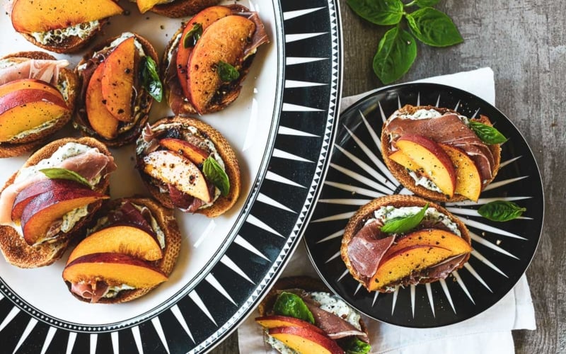 peach and prosciutto crostini on black and white plates