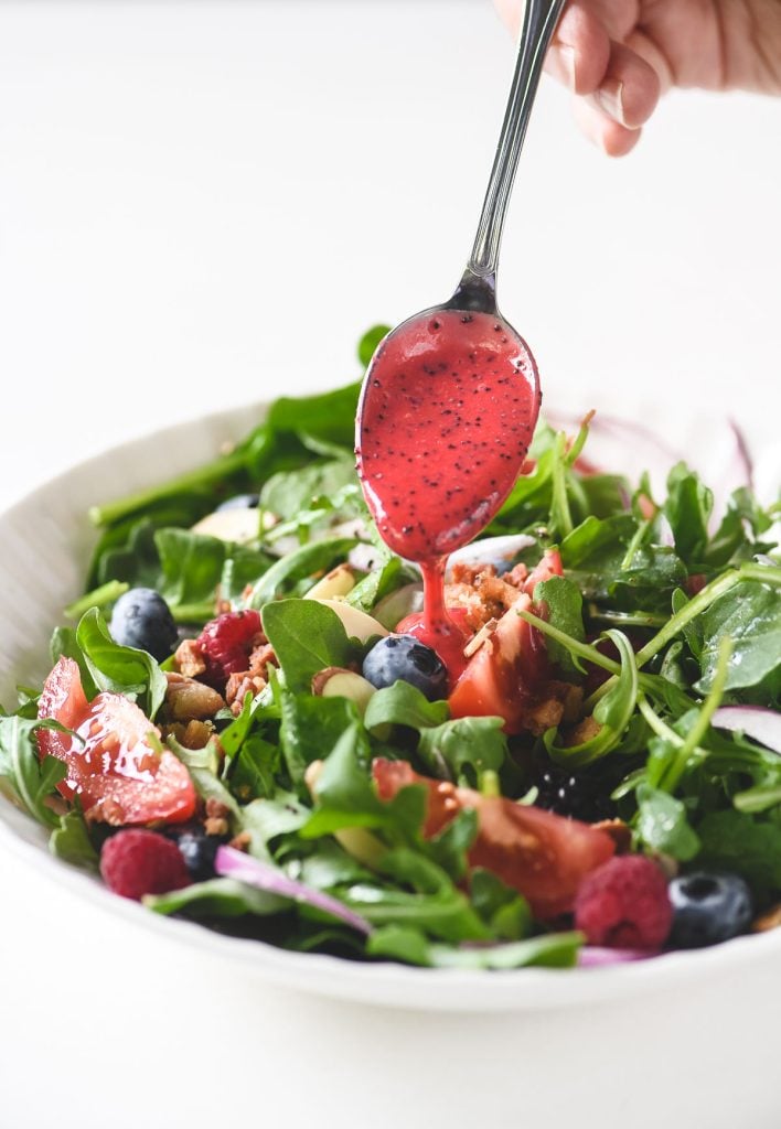spooning raspberry poppy seed dressing over a salad