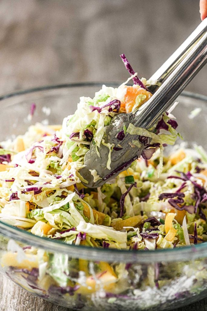 tossing coconut pineapple slaw with tongs