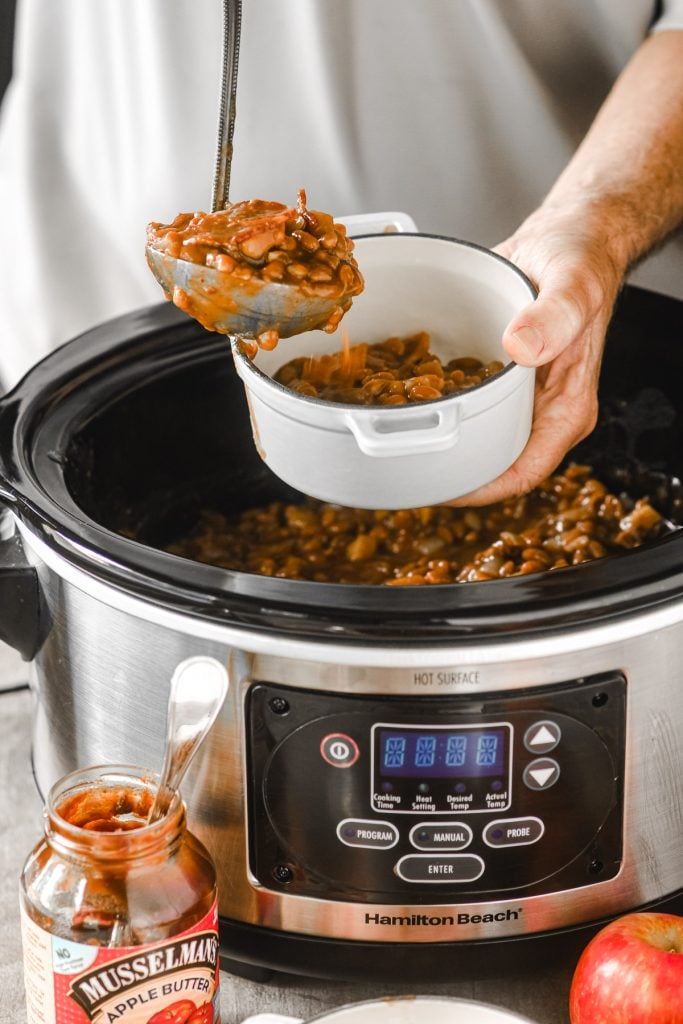 Ladling slow cooked apple butter baked beans into a bowl.