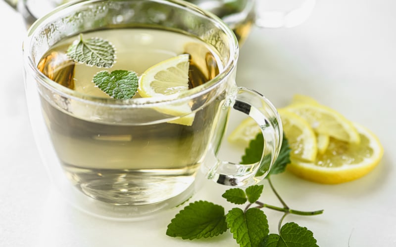 a cup of lemon balm tea with lemon wedge and lemon balm leaves.