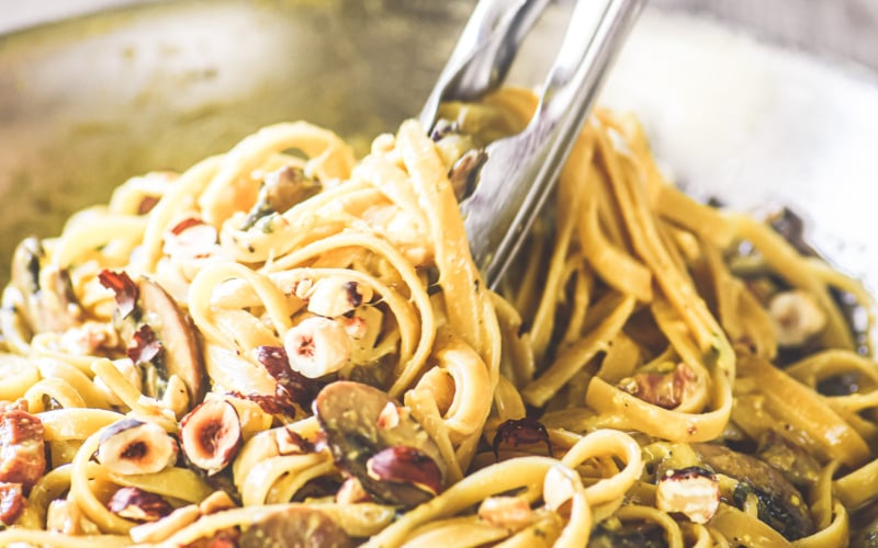 mushroom carbonara in a skillet with tongs