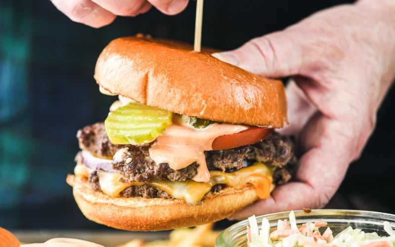 Holding a sheet pan smash burger with toothpick.