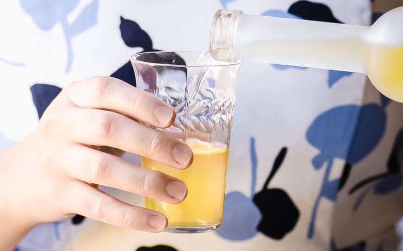 pouring homemade limoncello into a glass.