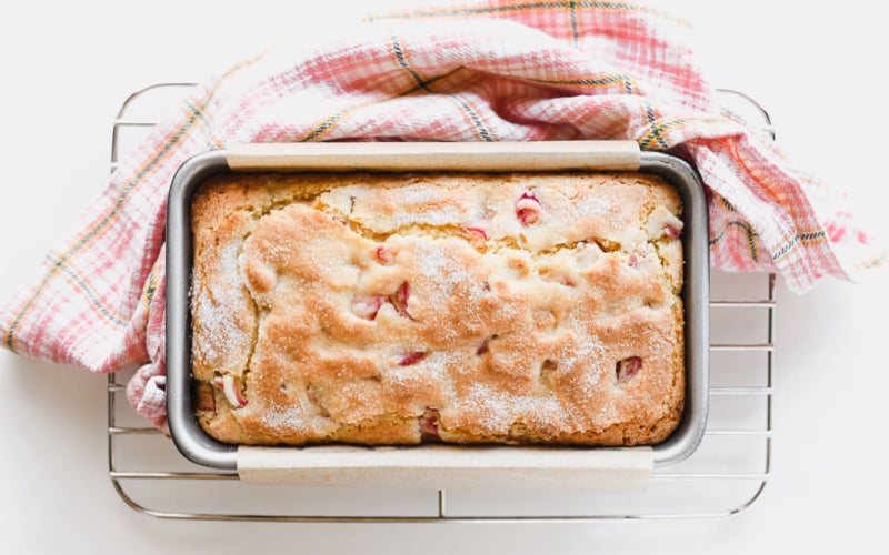 rhubarb bread on a cooling rack with dish towel.