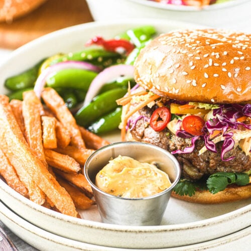 Chili Crisp Burgers with Asian Slaw on a plate with snap pea salad and sweet potato fries.