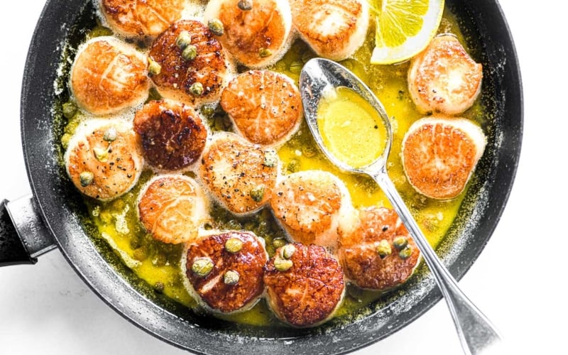 Seared scallops in lemon butter, in a skillet with spoon.