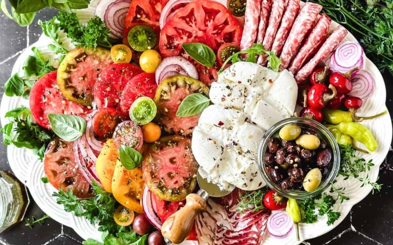 Burrata platter with tomatoes olives and sliced meats.