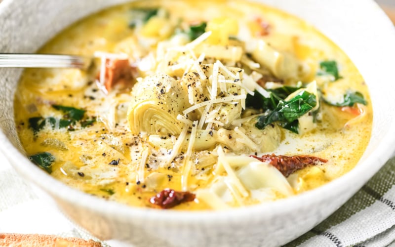 Tuscan artichoke soup in a bowl with chredded cheese.