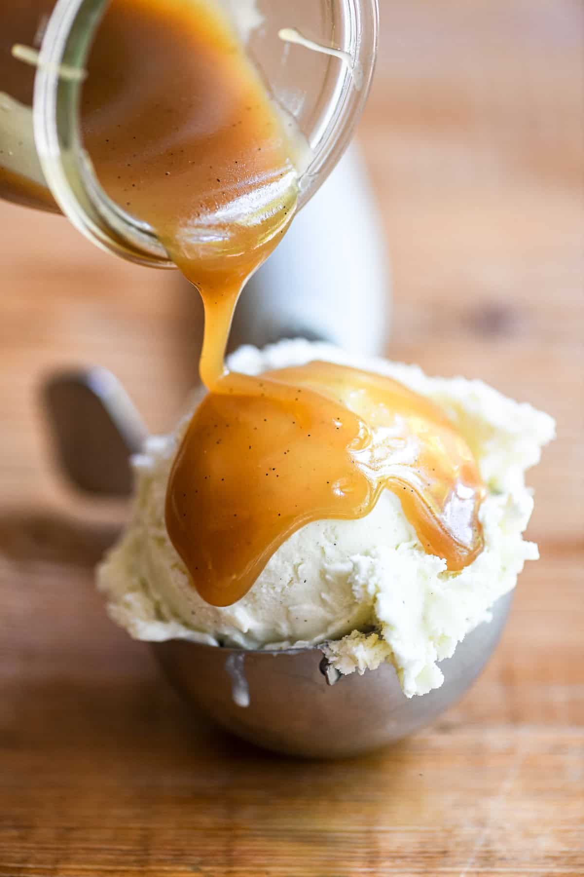 pouring butterscotch sauce over vanilla ice cream in an ice cream scoop.