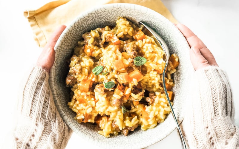 Holding a bowl of butternut squash risotto with sausage and sage.