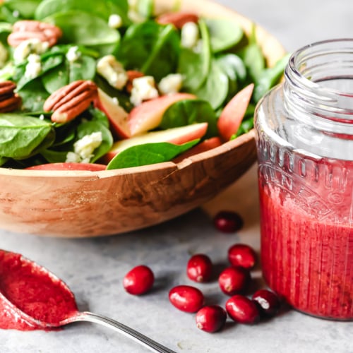 Cranberry vinaigrette in a small jar with spinach salad.