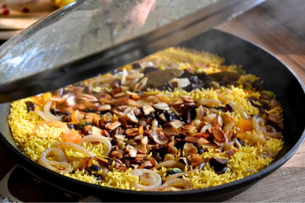 Persian Jeweled Rice is a gluten free, vegan rice pilaf topped with colorful gem-like fruits and nuts ~ this popular wedding dish is gorgeous! #easy #recipe #authentic #vegan #glutenfree #iranian #traditional #wedding #middleeastern #basmati #saffron #Christmas #passover #Easter Thanksgiving Opening the lid on a pot of Persian jeweled rice, with steam rising.