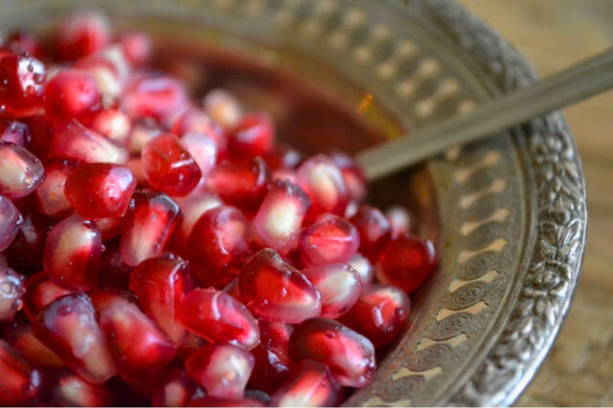 Red pomegranate seeds in a silver bowl.