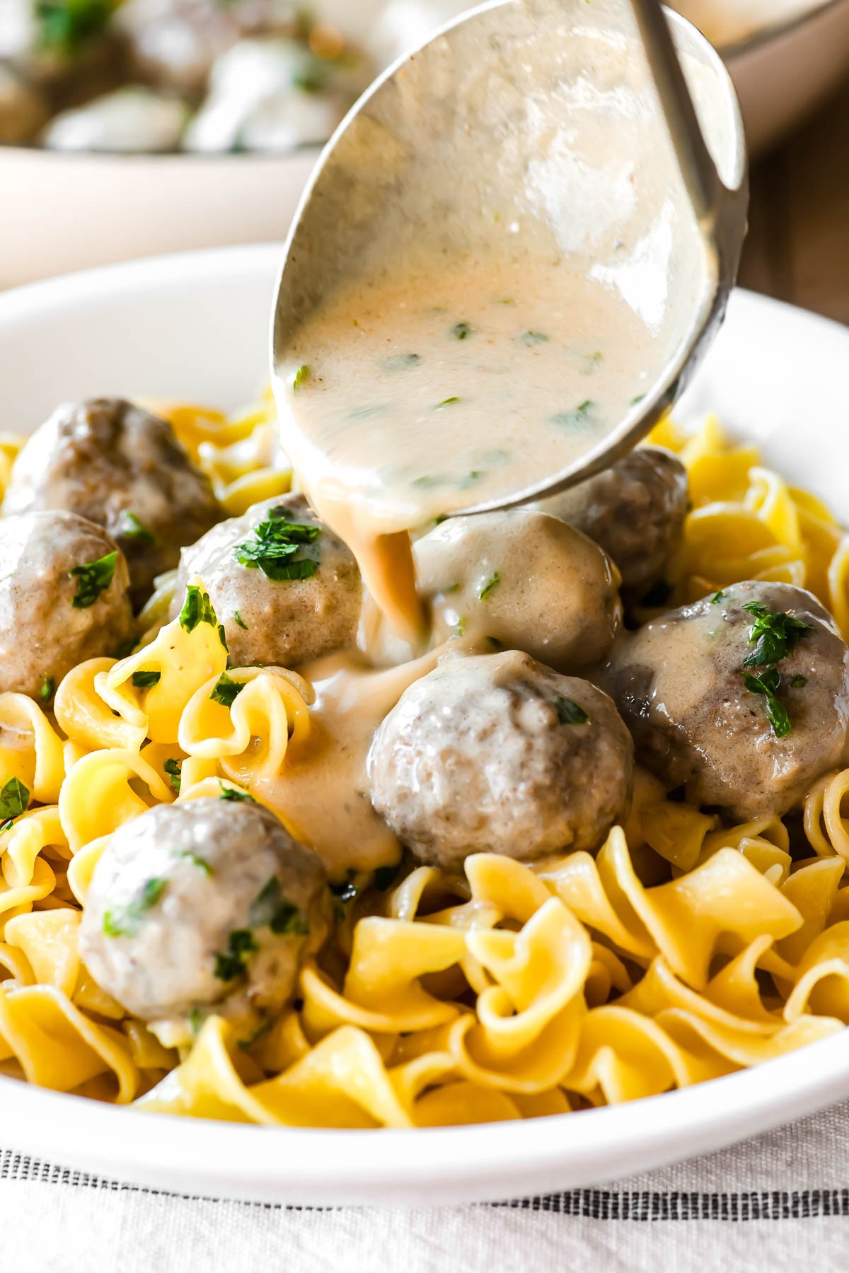 Ladling gravy over Swedish meatball noodle bowl.
