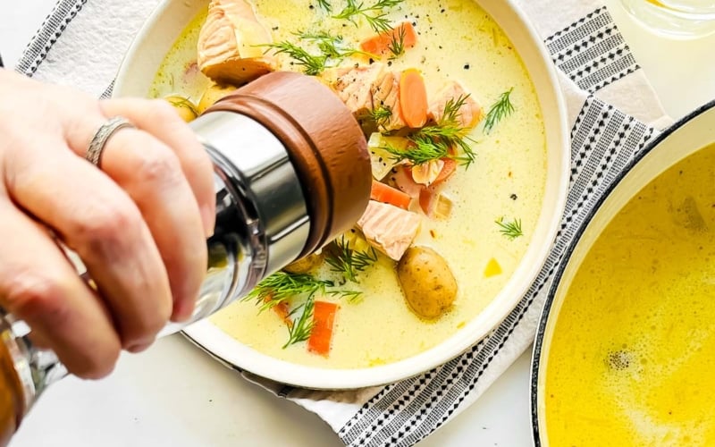 Adding fresh cracked black pepper to creamy lemon salmon soup.