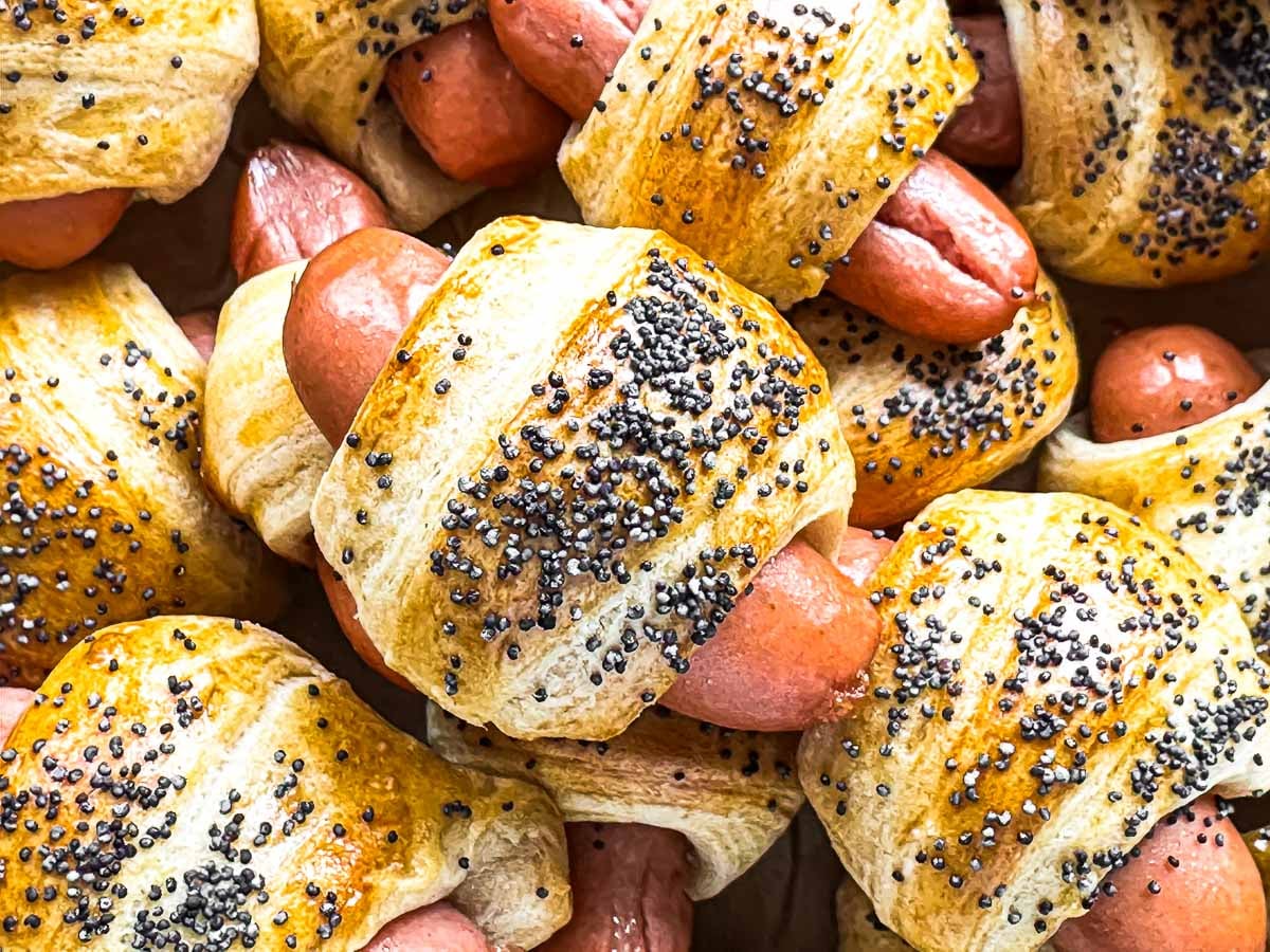 Golden brown pigs in a blanket topped with poppy seeds.