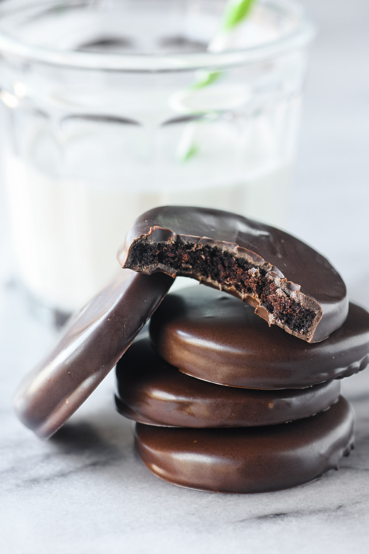Homemade Thin Mint cookies, stacked next to a glass of milk with a green straw.