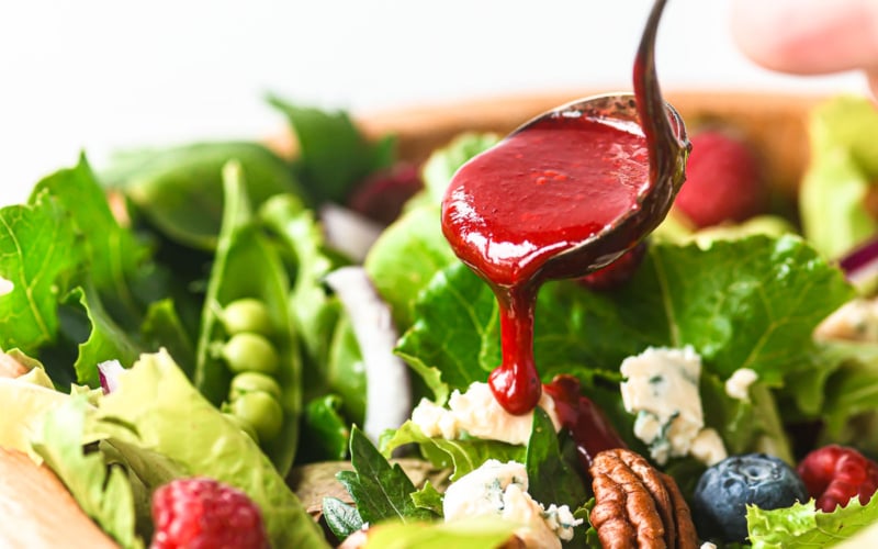 Spooning black raspberry vinaigrette dressing onto a summer berry salad.