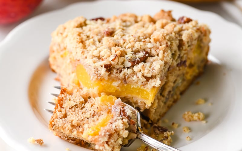 A slice of butter pecan peach cake with fork taking a bite.