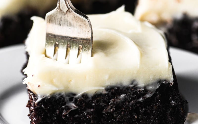 chocolate zucchini snack cake with cream cheese frosting with fork in it.