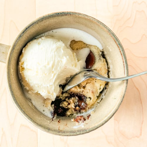 cookie in a mug with melting ice cream and spoon.