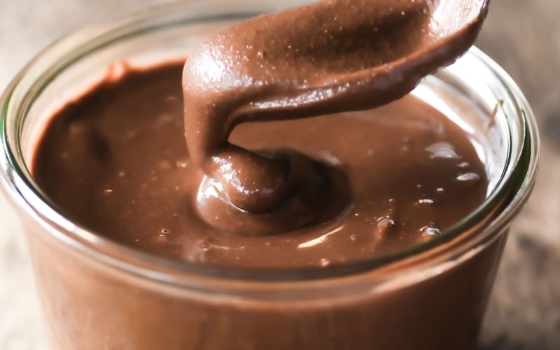 Dipping a spoon into a small glass jar of homemade Nutella.