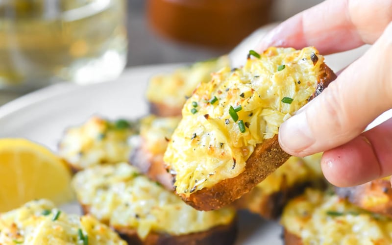 Taking an artichoke Parmesan crostini from a plate.