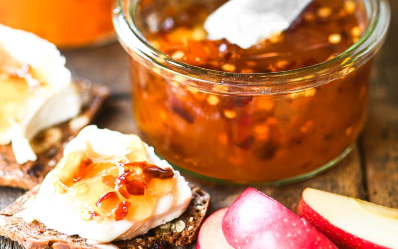 A jar of apple hot pepper jelly with soft cheese and crackers.