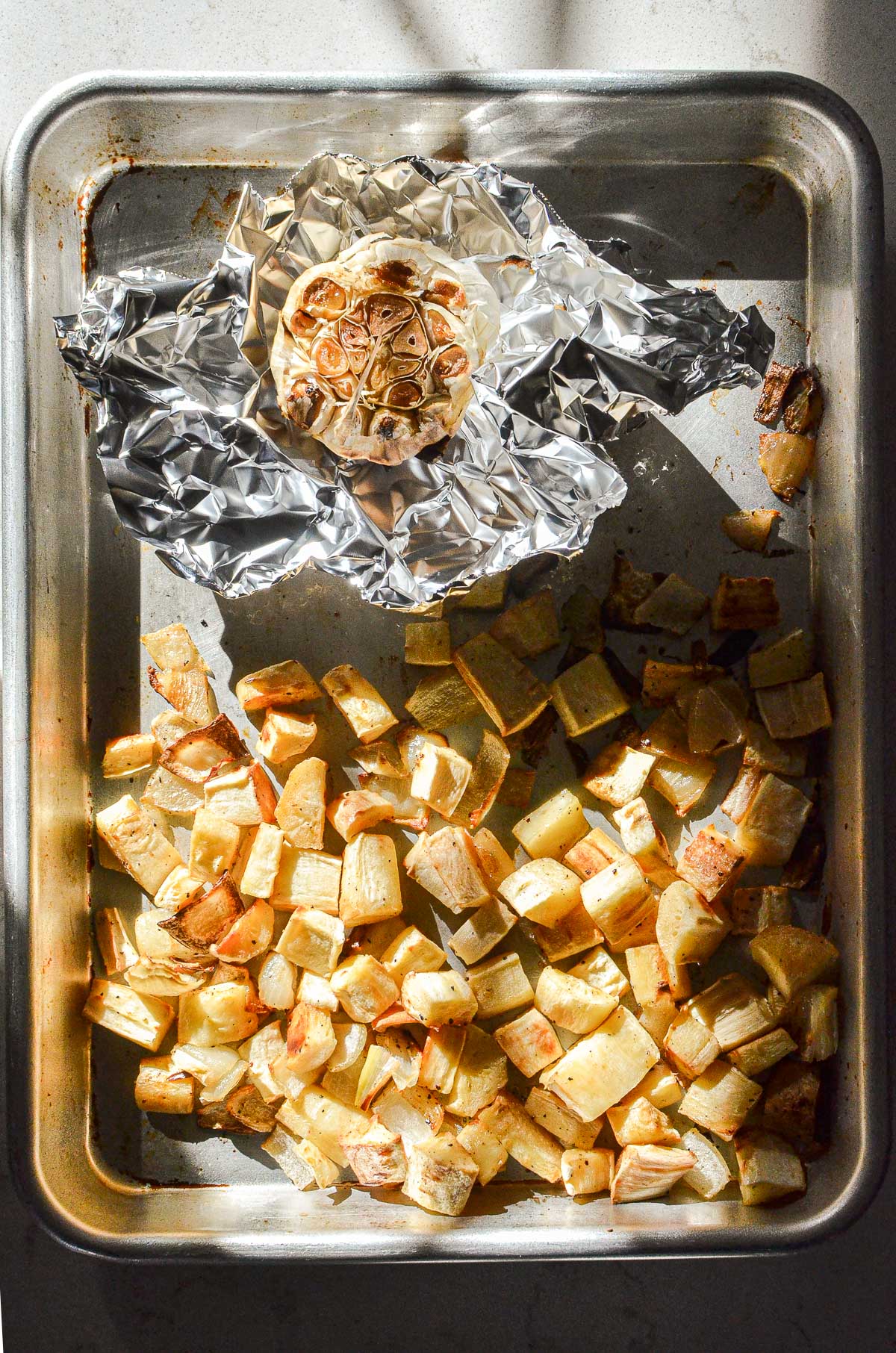 A baking sheet with roasted parsnips and onions, and roasted garlic in foil. 