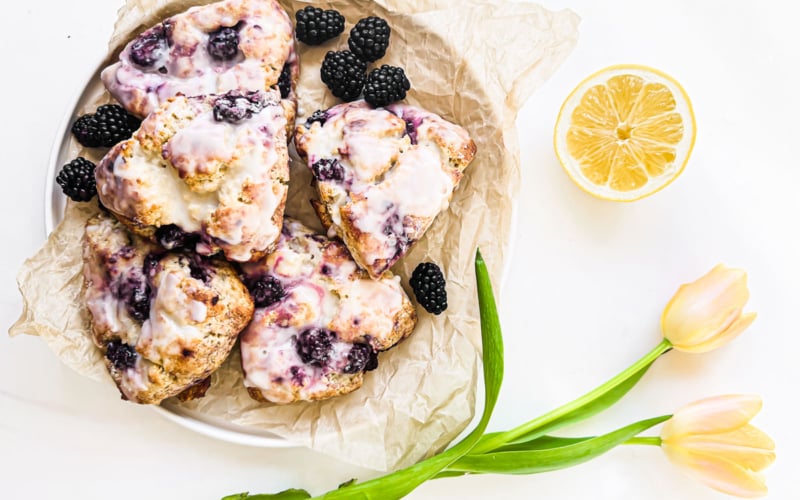 blackberry lemon scones on a plate with blackberries, lemon and tulips.