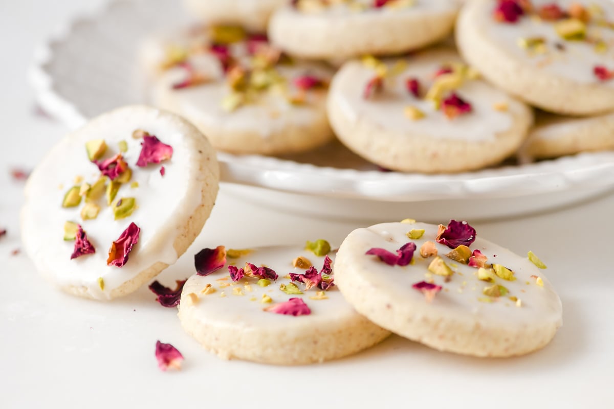 Persian Love Cookies on a white counter, topped with rose petals and crushed pistachios.