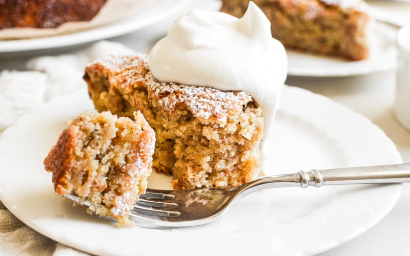 taking a bite of a slice of almond flour banana cake, topped with whipped cream.