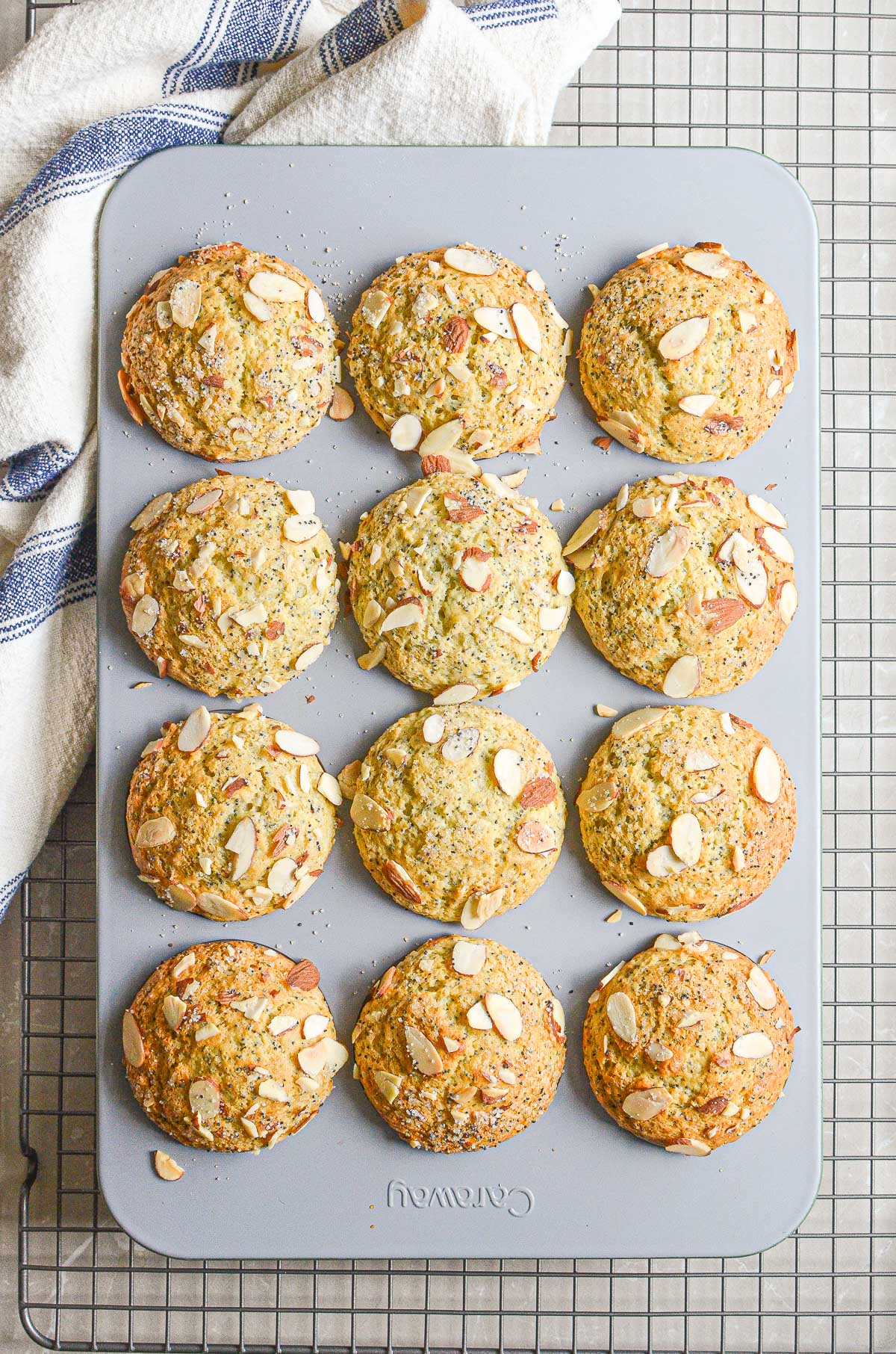 A muffin pan of almond poppy seed muffins on a baking rack.