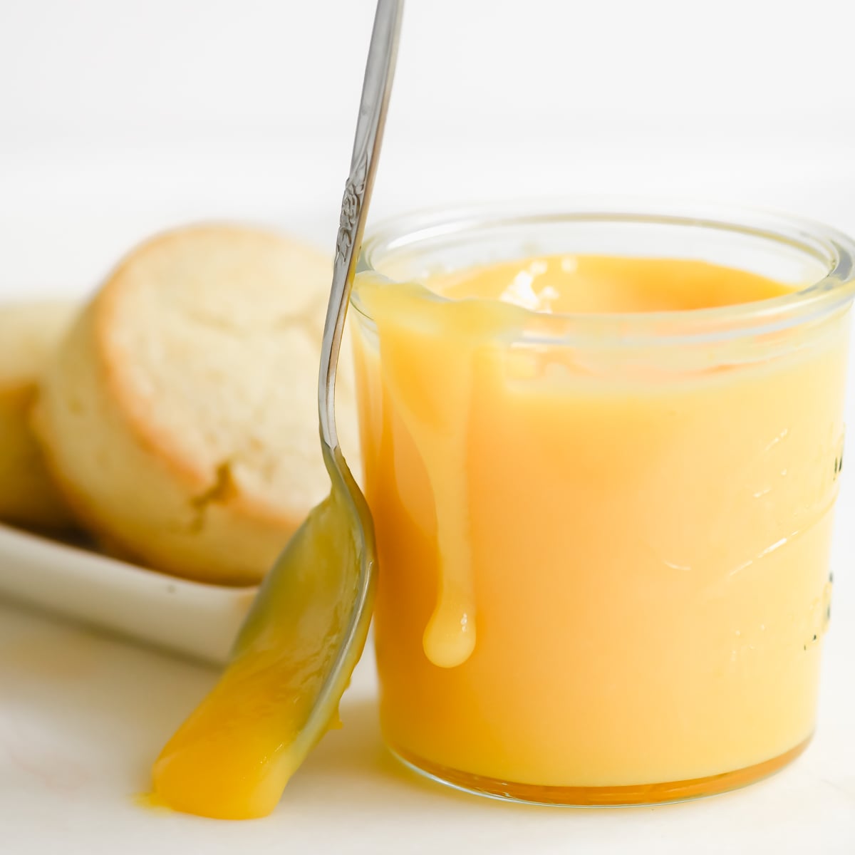 a jar of microwave lemon curd with scones on a plate.