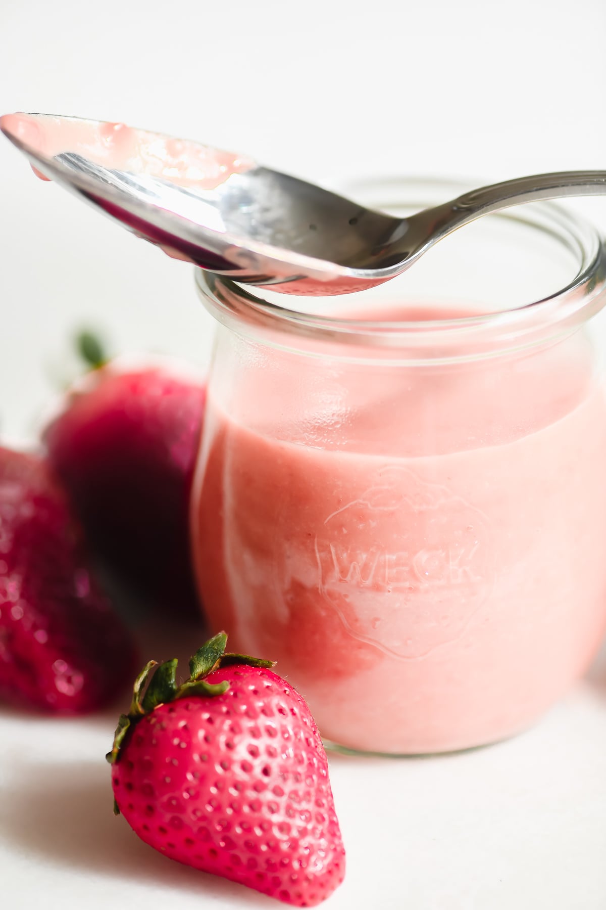 a spoon on top of a small jar of strawberry curd.