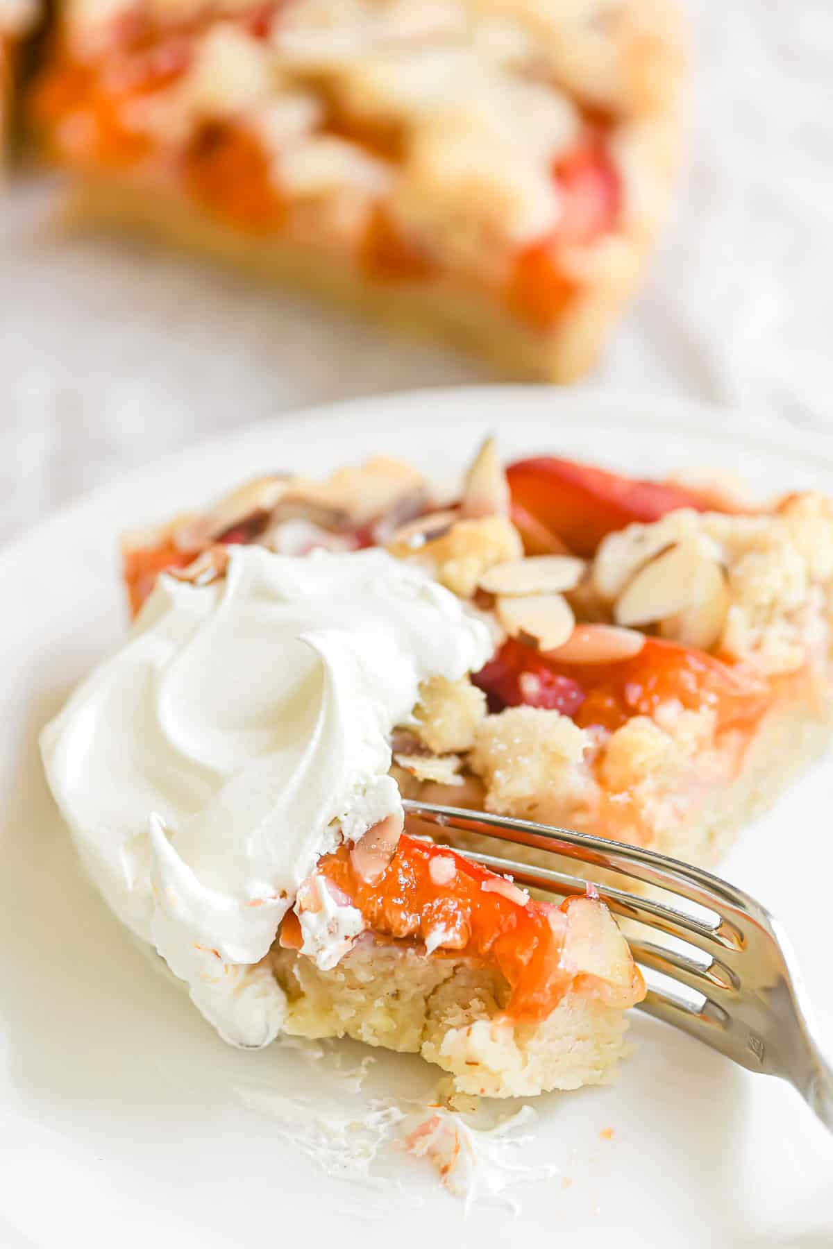A fork taking a bite of apricot almond tart topped with whipped cream.