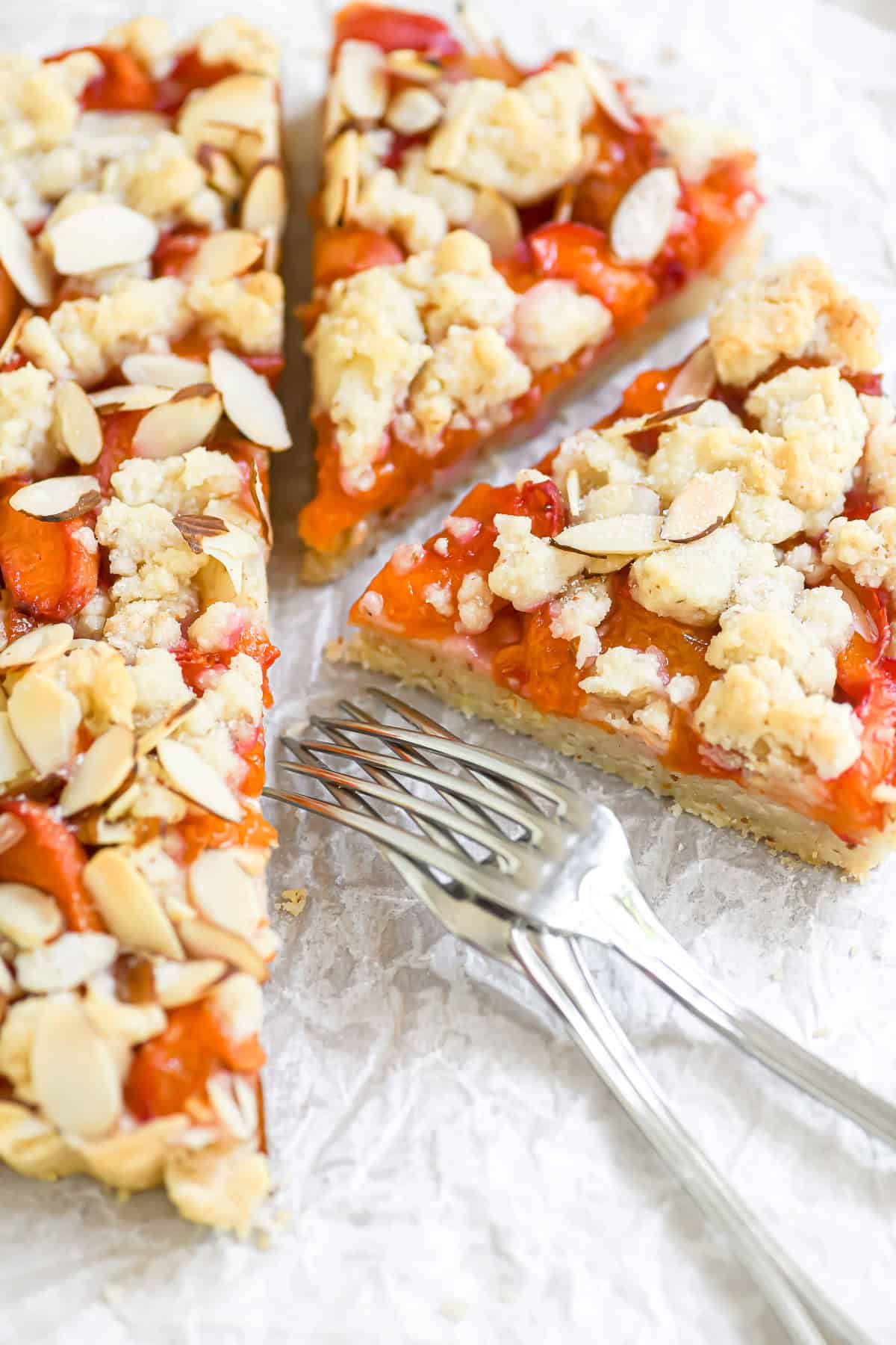 An apricot almond tart on parchment paper with forks.