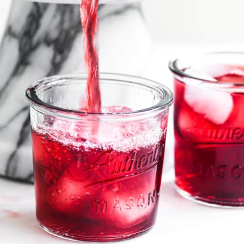 Pouring a glass of red hibiscus tea from a drink dispenser.