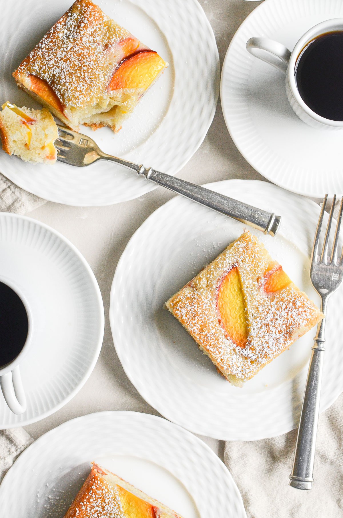 Almond peach cake slices on white plates, with cups of espresso.