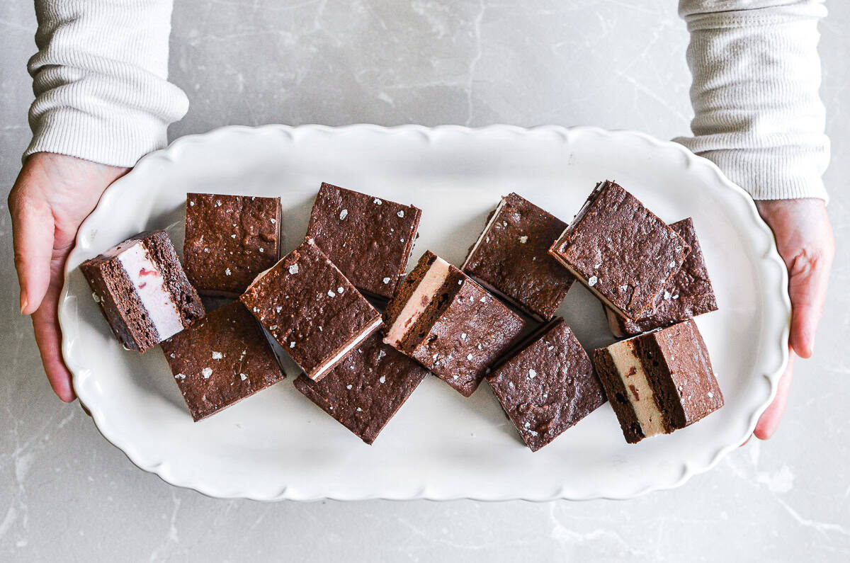 Hands holding a tray of brownie ice cream sandwiches.
