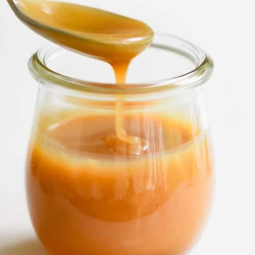 Honey caramel Sauce dripping from a spoon in a small glass Weck jar.