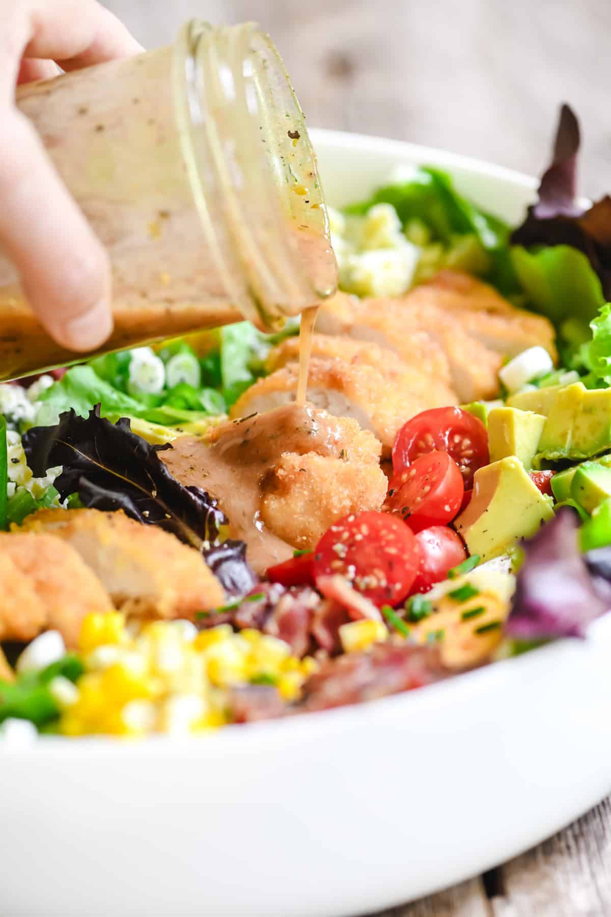 pouring red wine vinaigrette dressing onto fried chicken cobb salad.