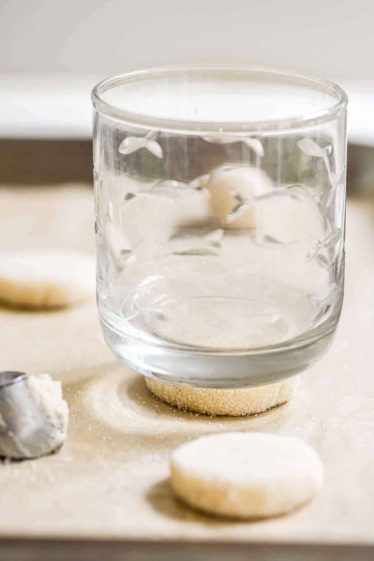 A ball of thin and crispy sugar cookie dough being flatteend with a glass.