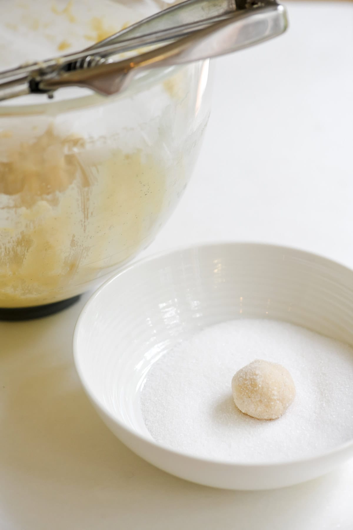 a ball of thin and crispy sugar cookie dough in a bowl of sugar.