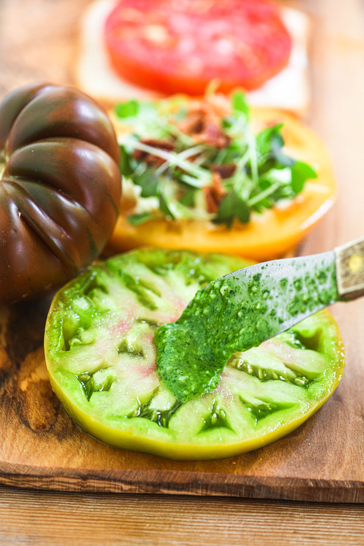 spreading homemade pesto on a slice of tomato.