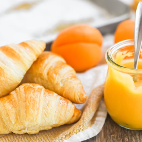 a small jar of apricot curd with fresh baked croissants.