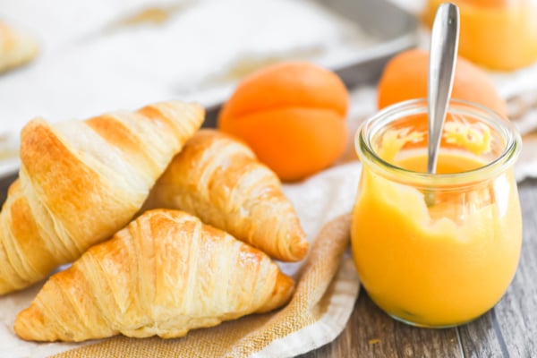 a small jar of apricot curd with fresh baked croissants.