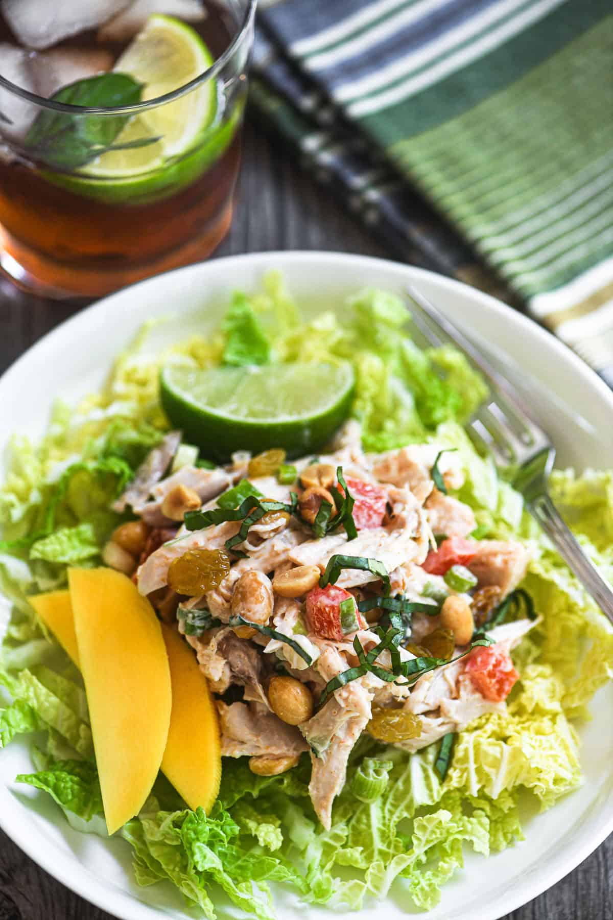 Thai curry chicken salad on a white plate with lime and mangoes.
