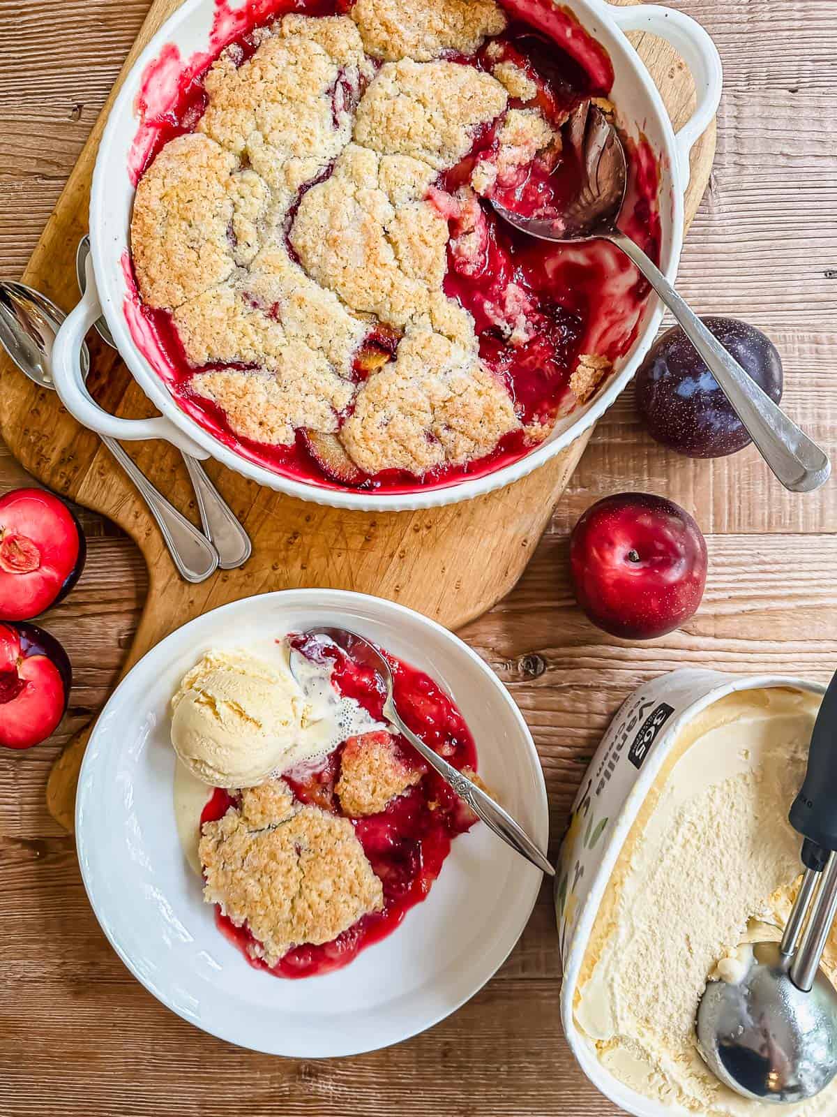 Plum cobbler in a white casserole with ice cream.